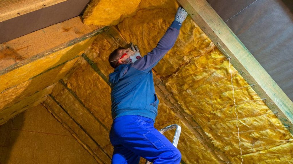 Een man brengt minerale wol aan in het regelwerk van een schuin dak. 